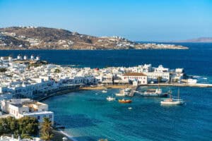 A yacht harbor of Mykonos, with blue water, white buildings, and windmills.